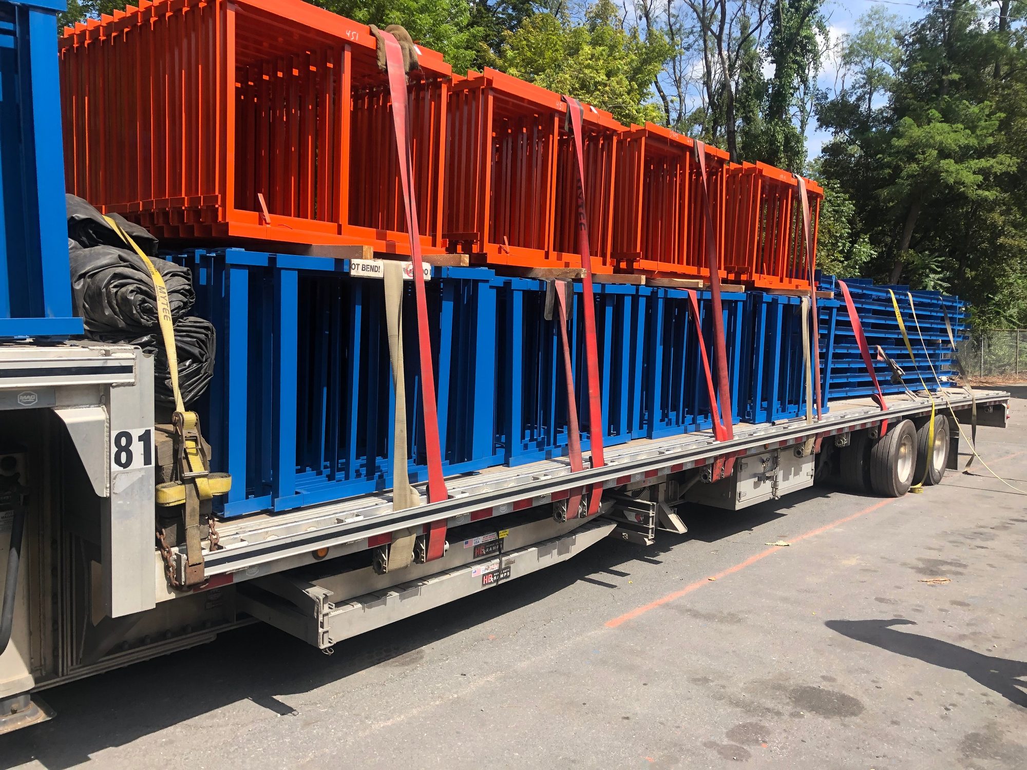 Orange and blue fabricated steel frames loaded and strapped on a flatbed trailer